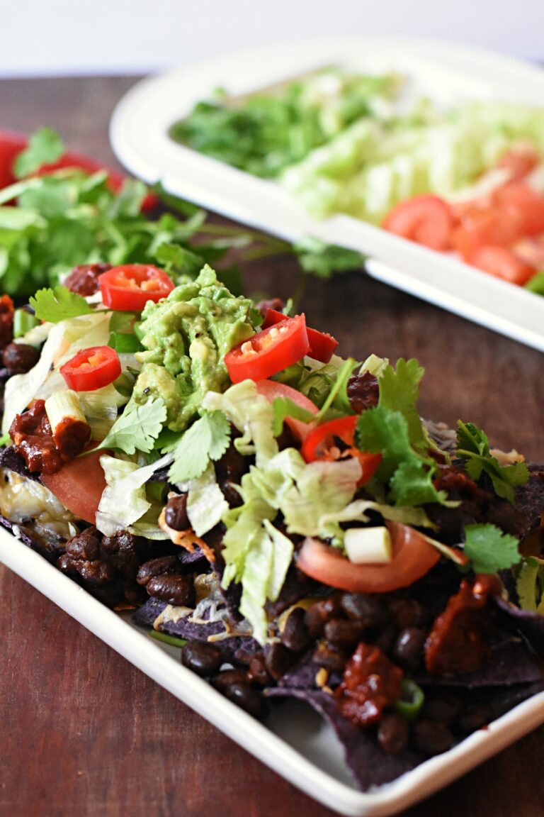 Purple tortilla chips topped with black beans, lettuce, mashed avocado and chili pepper slices and chopped cilantro.