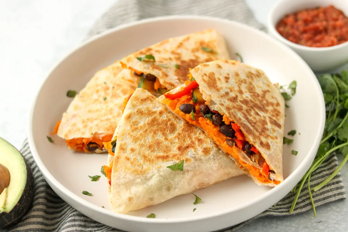 Stuffed tortilla triangles are placed on a white plate. Sweet potato and black bean filling is visible