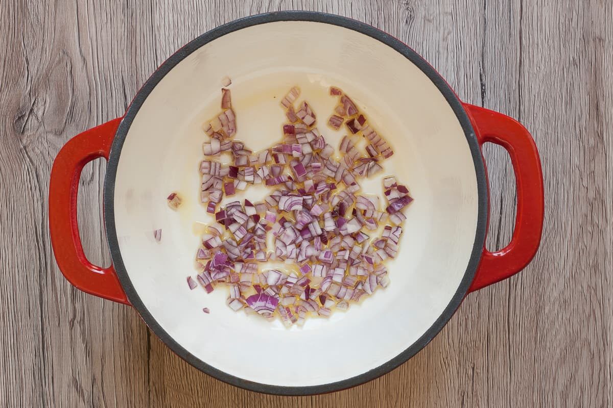 White red enameled Dutch oven with chopped red onion. 