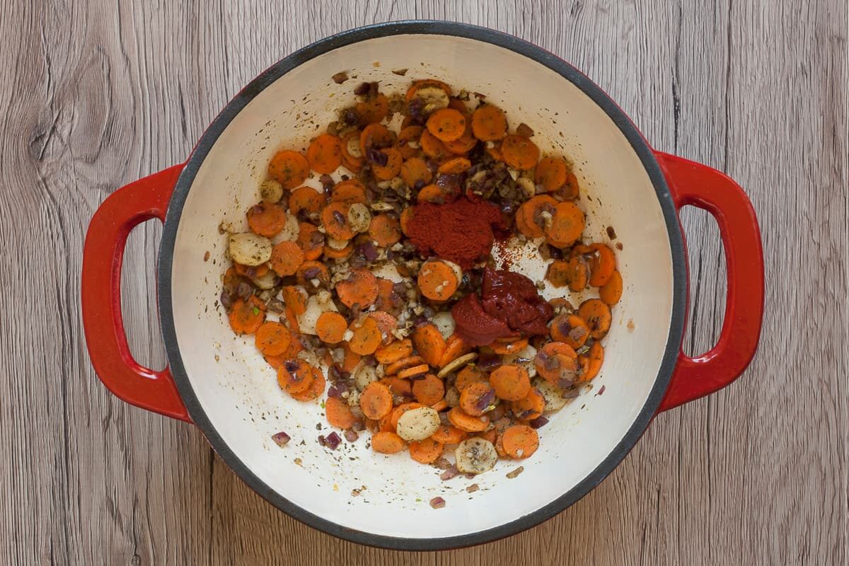 White red enameled Dutch oven with mixed chopped red onion, carrot, parsnip slices and green herbs.