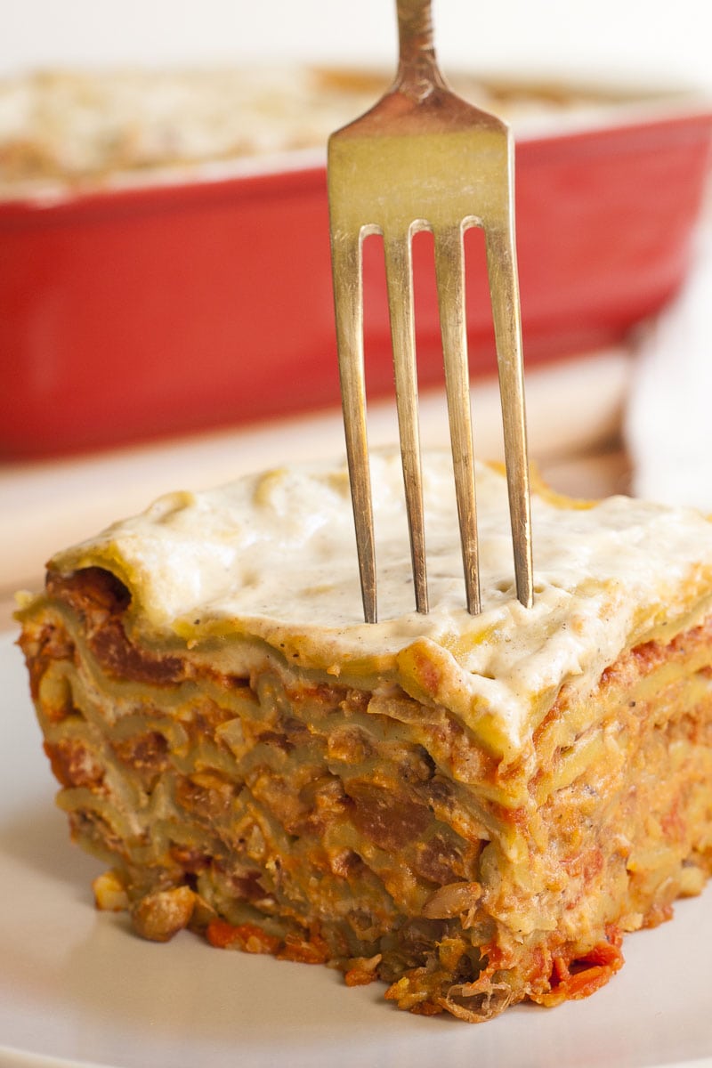 A slice of vegan lasagna and a fork which takes the first bite. 
