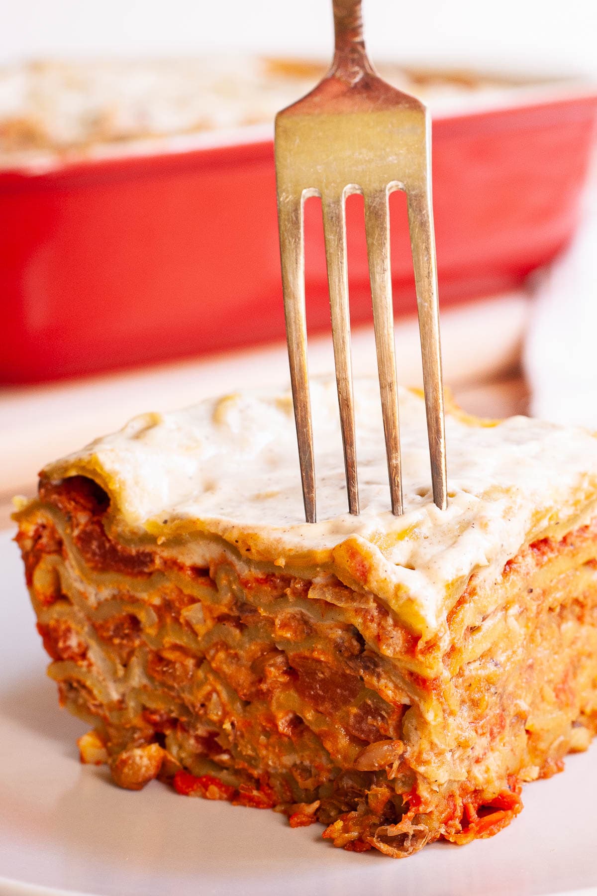 A slice of layered lasagna is on a plate. A fork is piercing through the middle.