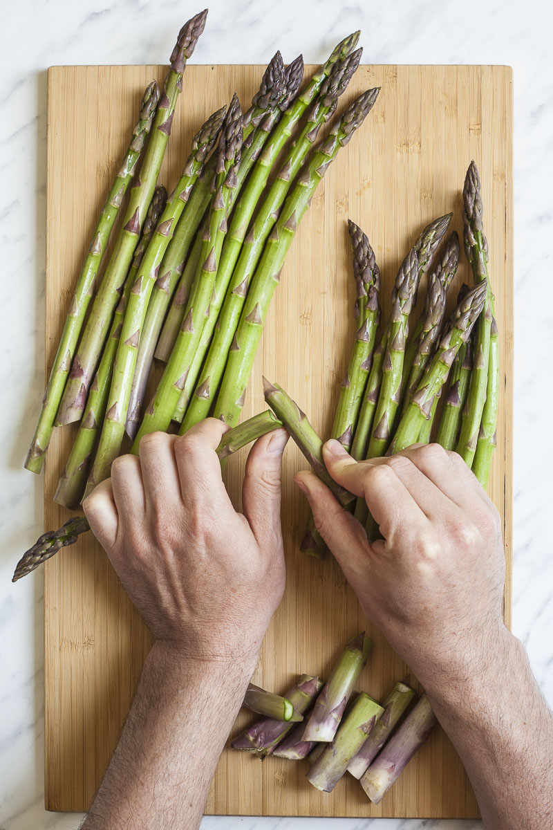 Wooden board with asparagus. A hand is snapping the end of asparagus