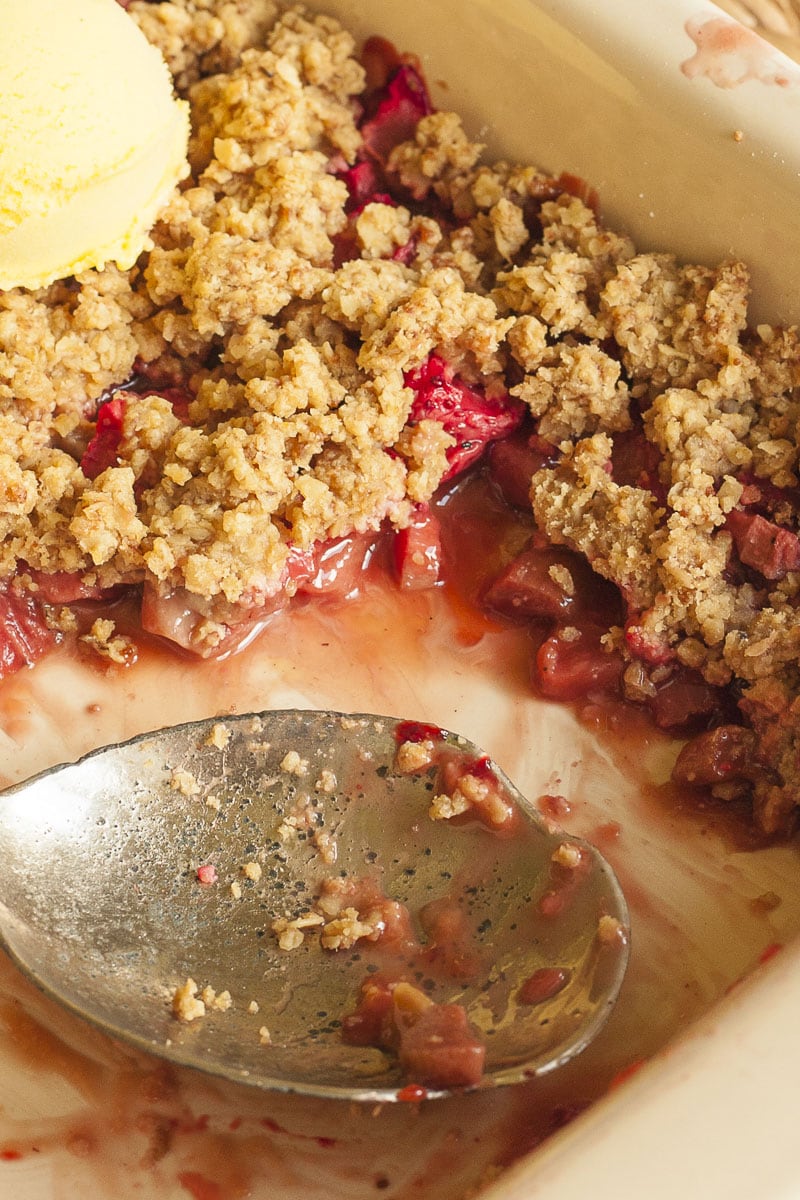 A white baking dish with red fruity sauce and brown crisp up close with a serving spoon in the middle