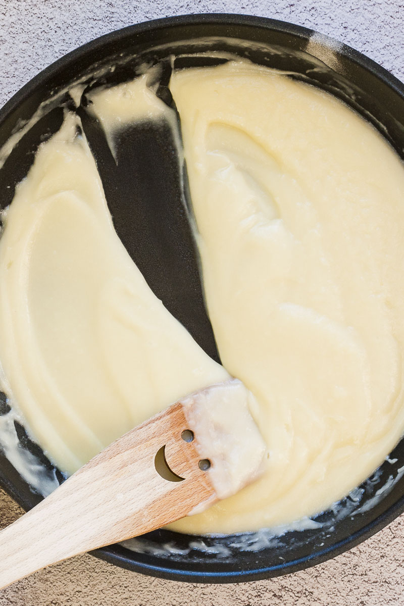 White sauce in frying pan and a wooden spatula is making a dent