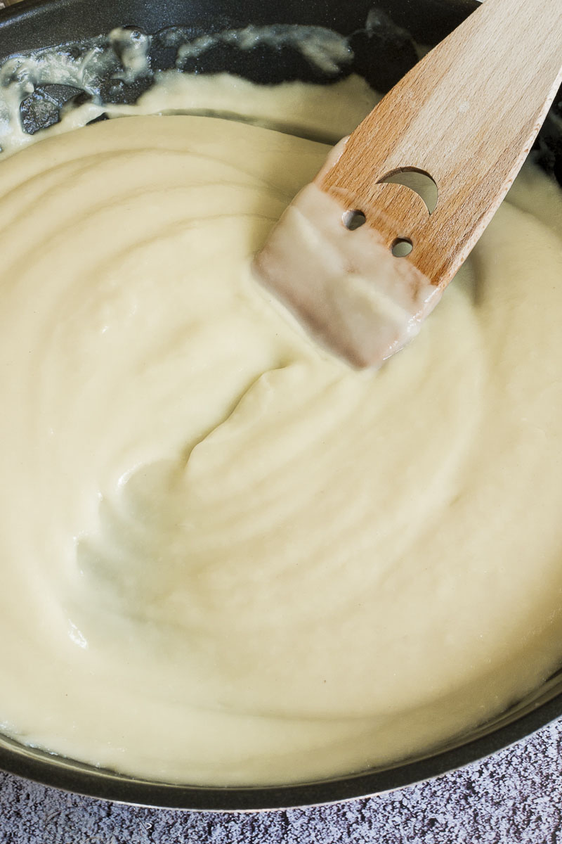 White sauce in black frying pan with a smiling wooden spatula in the middle