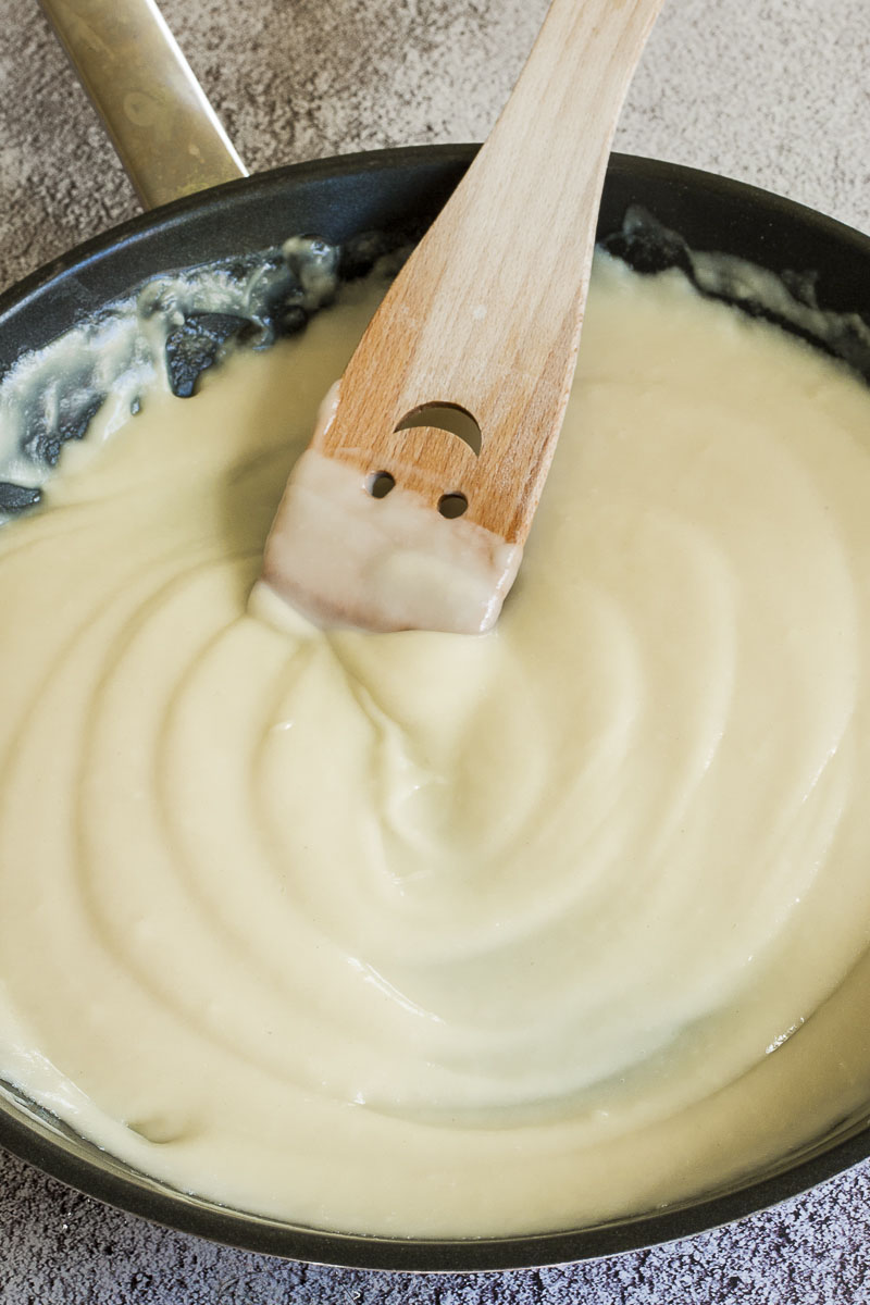 White sauce in black frying pan with a smiling wooden spatula in the middle