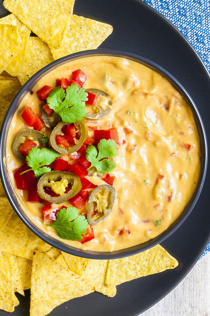 Yellow sauce in a black bowl topped with red veggie chunks, sliced green pepper and green leaves of herbs. 