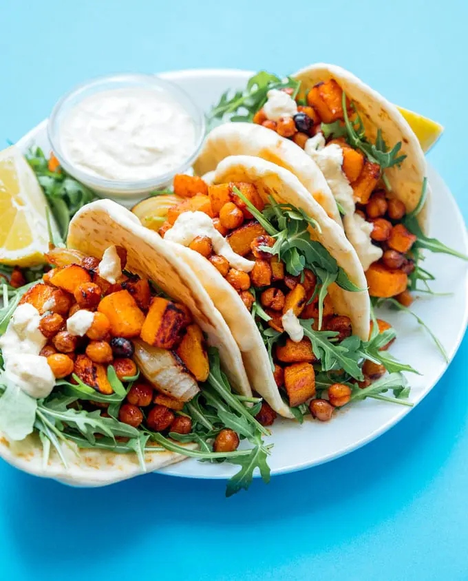 Pita tortillas folded in hald and stuffed with orange butternut squash, chickpeas and arugula and placed it on a white plate with blue background