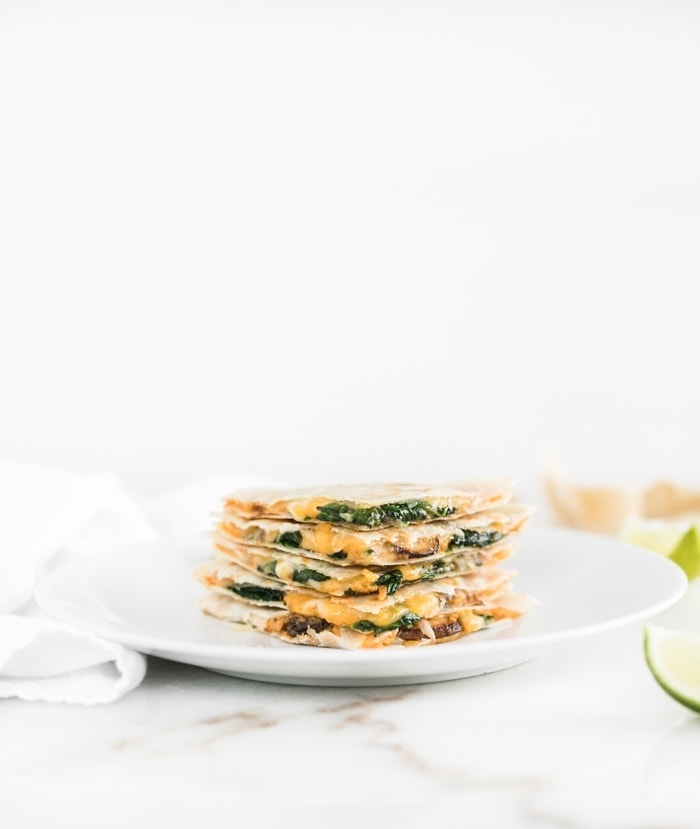 A stack of cut-up quesadilla slices stuffed with yellow sauce and wilted green veggies in between tortilla sheets. 