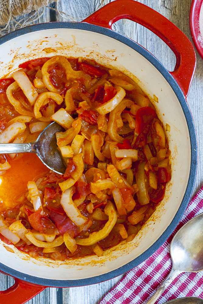 Red and yellow veggie stripes in a red stew in a red and white pot.