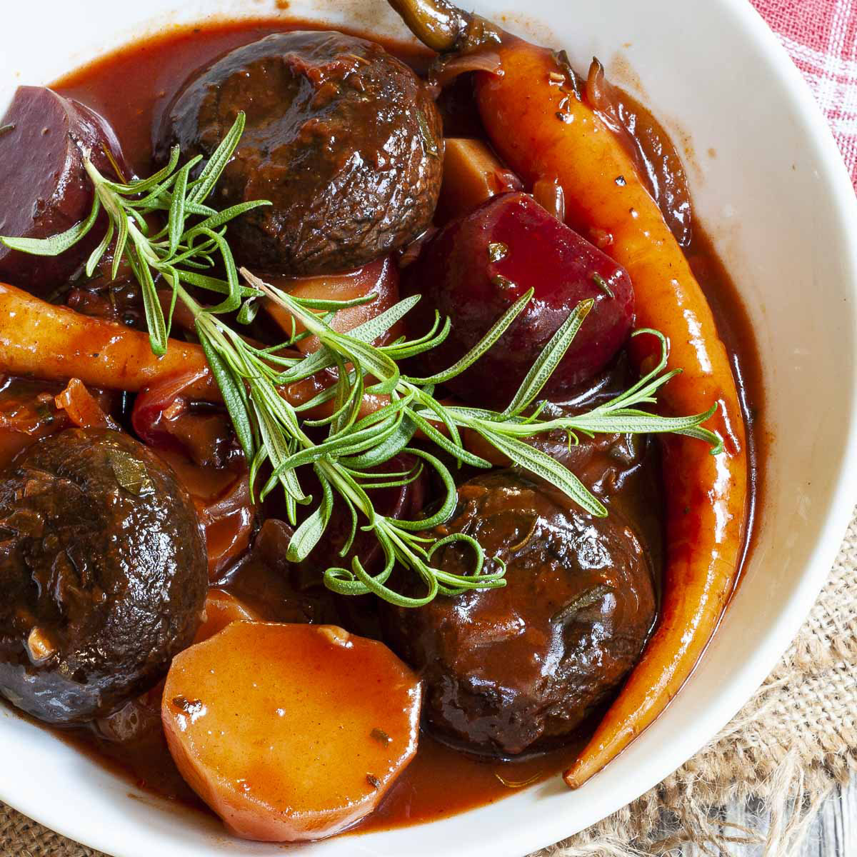 White plate with yellow, red, purple veggies and portobello mushroom caps topped with fresh green herbs on twigs