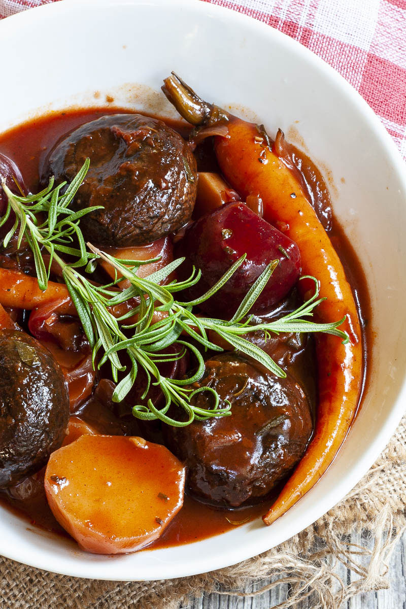 White plate with yellow, red, purple veggies and portobello mushroom caps topped with fresh green herbs on twigs