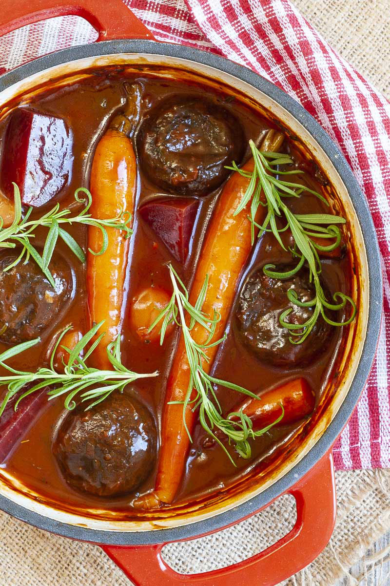 Red pot with yellow, red, purple veggies and portobello mushroom caps topped with fresh green herbs on twigs