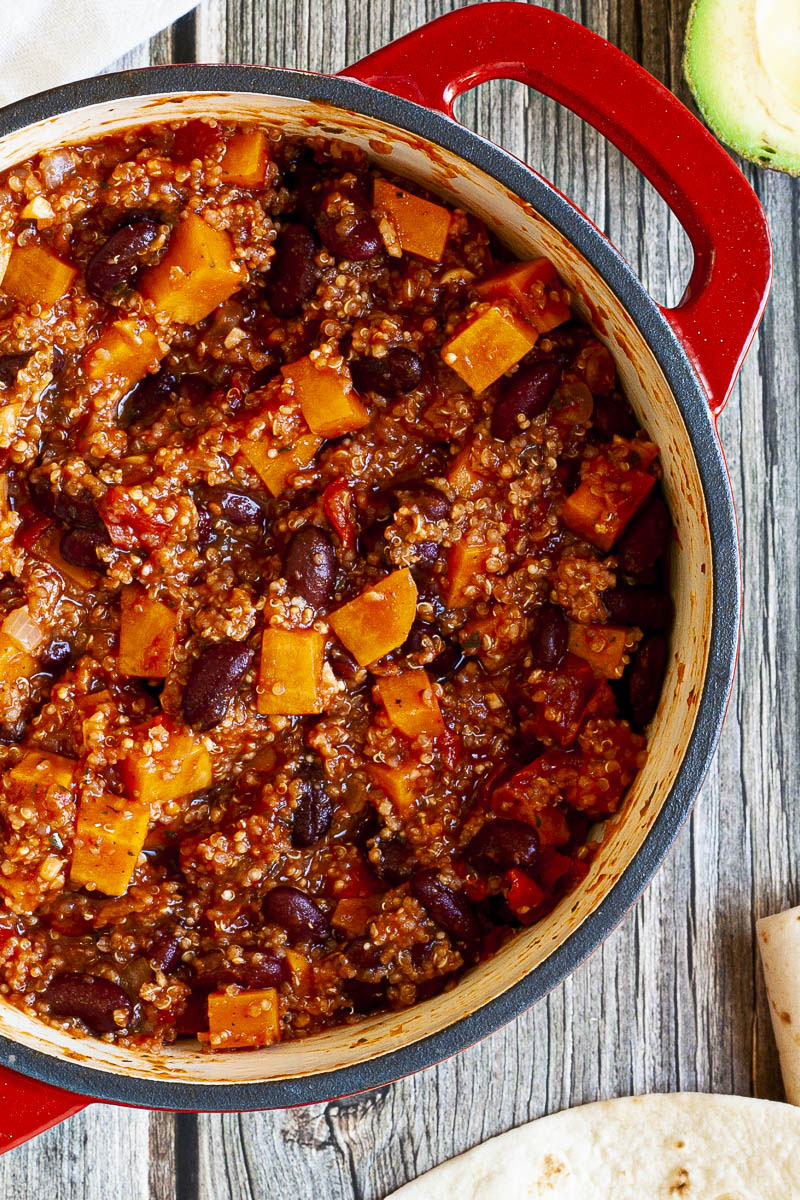 In a red dutch oven there are orange cubes, dark brown beans, small white, yellow seeds.