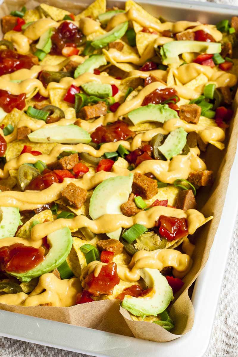 Silver sheet pan full of yellow tortilla chips, avocado slices, jalapeno slices, red and yellow sauce. 