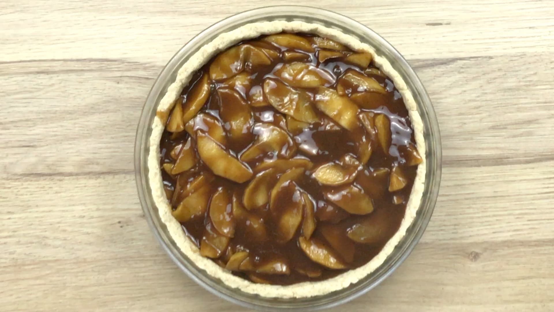 A pie crust in a glass pie pan filled with apple slices in caramel sauce.