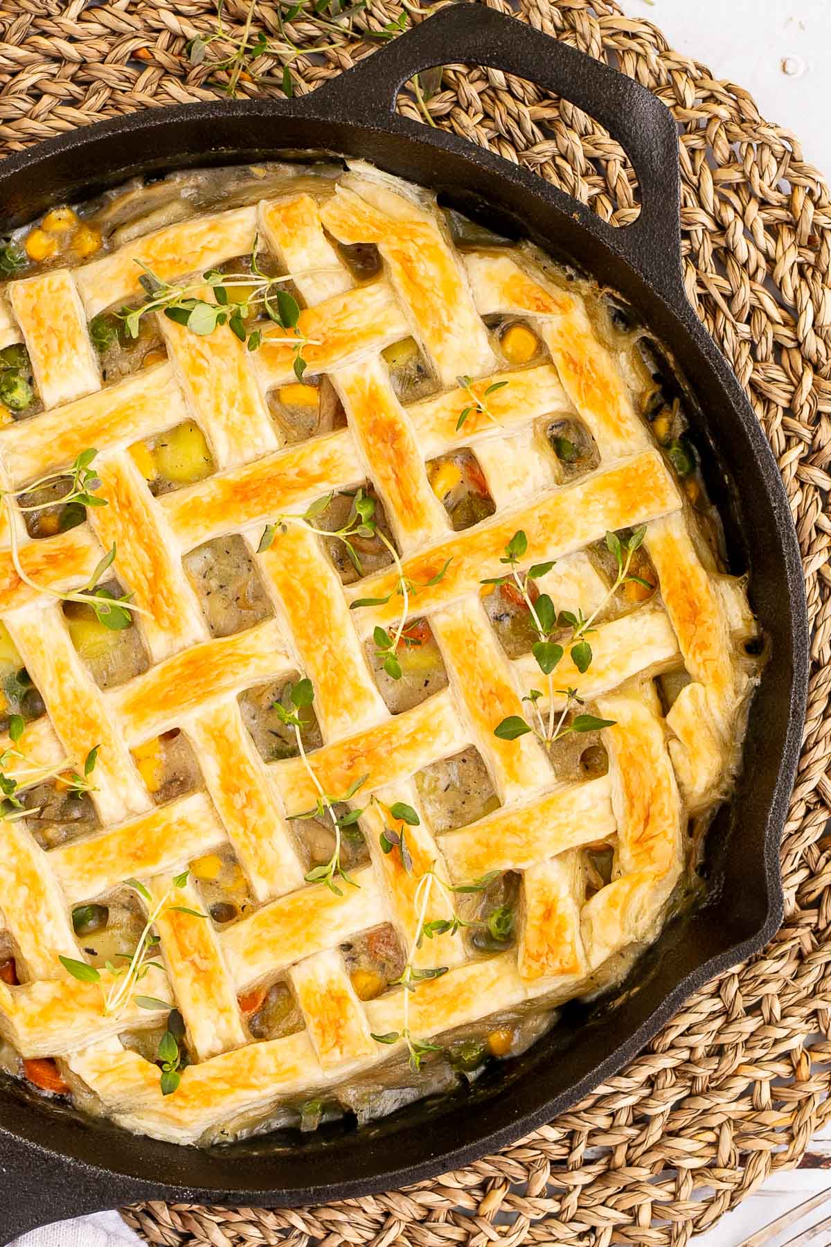 Cast iron skillet with veggie stew topped with puff pastry in a lattice pattern.