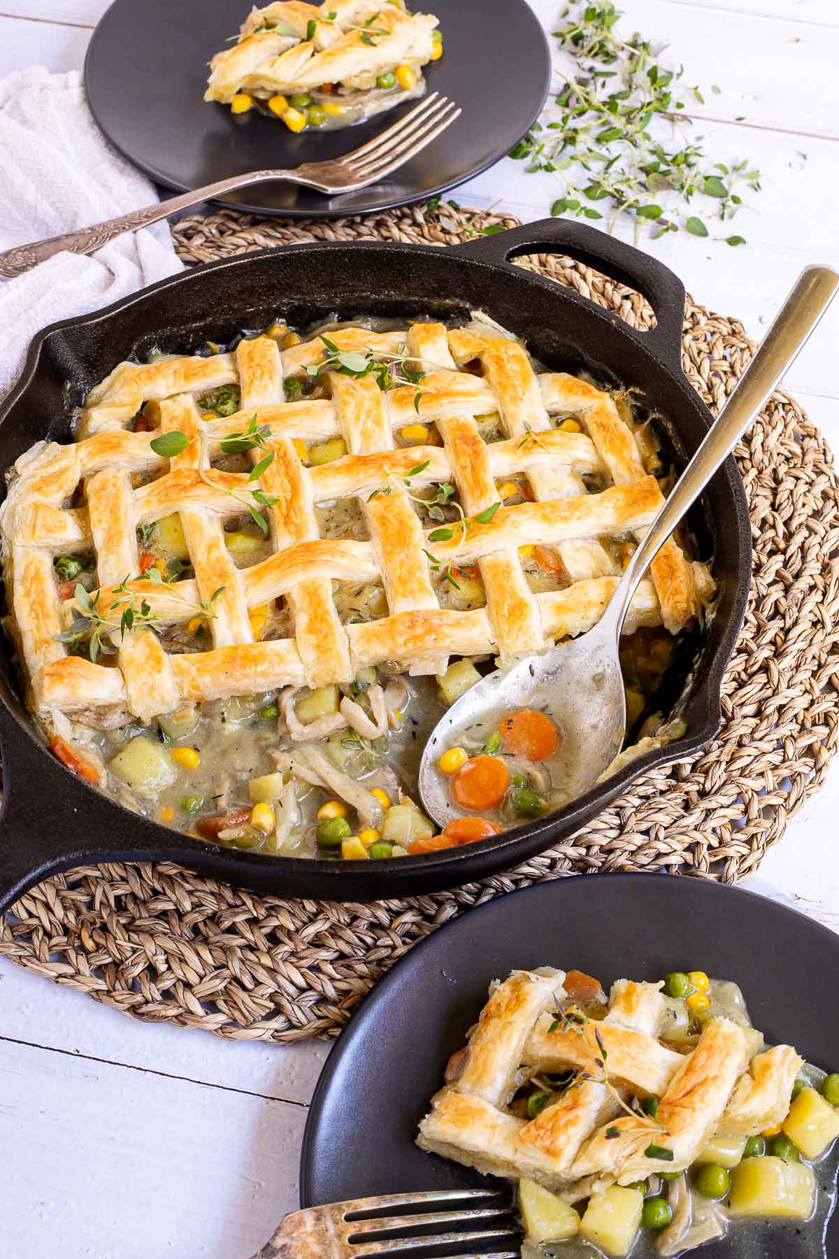 Cast iron skillet with veggie stew topped with puff pastry in a lattice pattern. A part of it is missing and the stew is visible next to the serving spoon.
