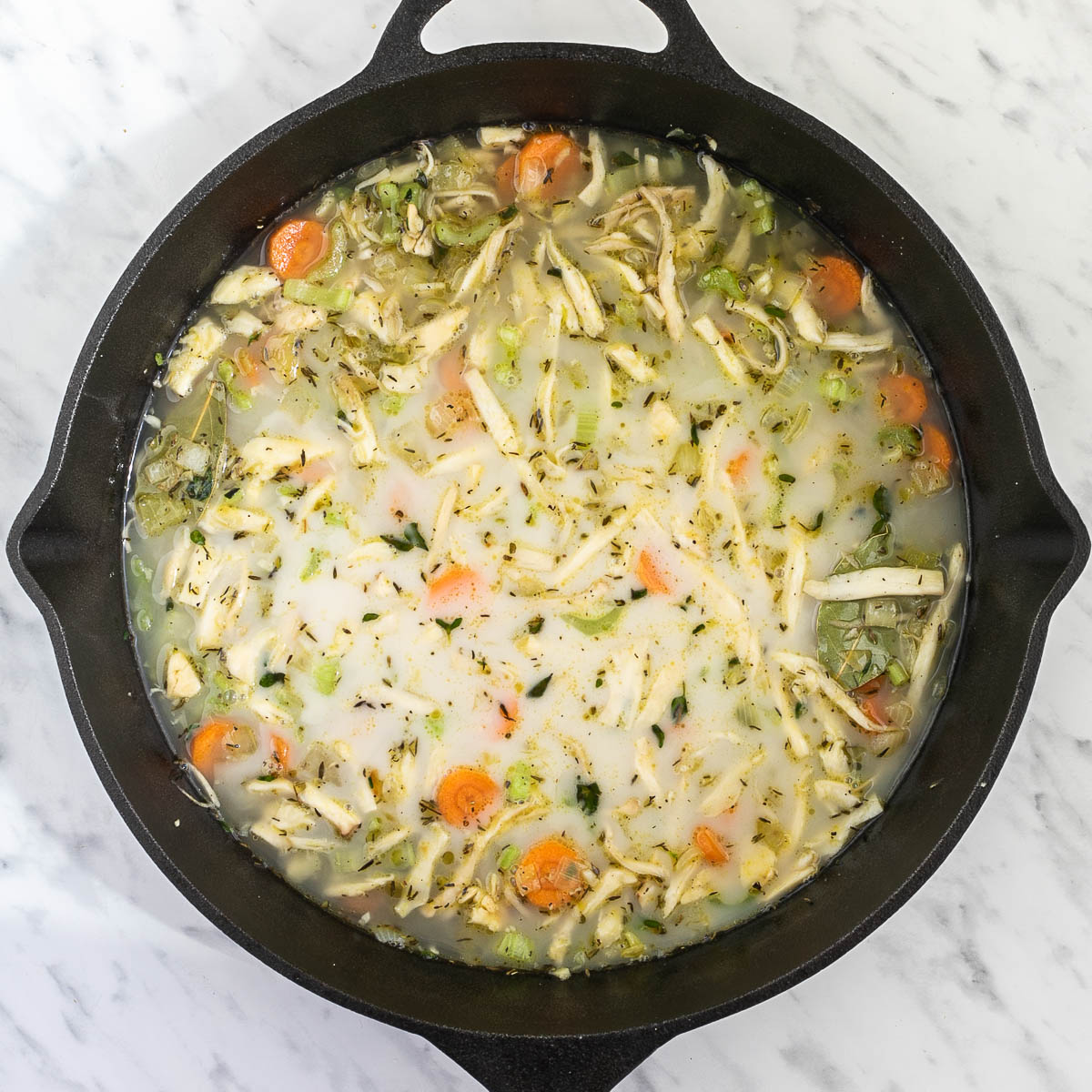 Cast iron skillet with light broth-like liquid with sliced carrots, chopped onion, garlic, celery, shredded king oyster mushrooms, bay leaves, and thyme.