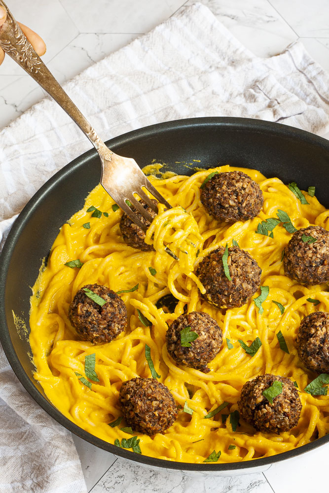 Yellow pasta sauce in a frying pan topped with mushroom meatballs.