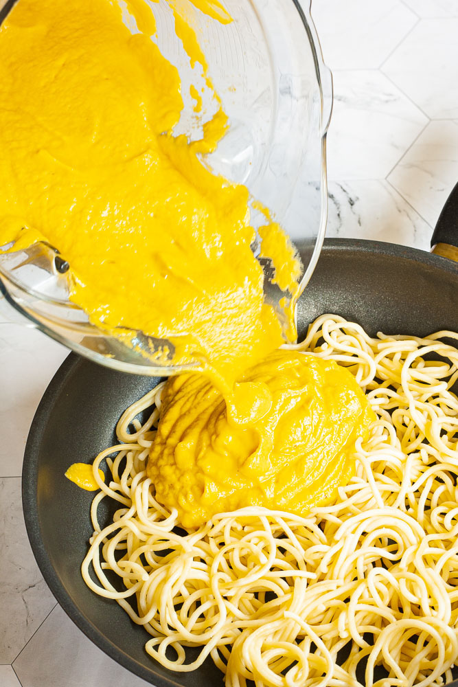 Yellow pasta sauce poured on top of spaghetti in a frying pan.