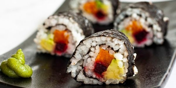 4 sushi rolls on a black plate. The rolls have black cover and white inside with purple yellow and green in the middle.