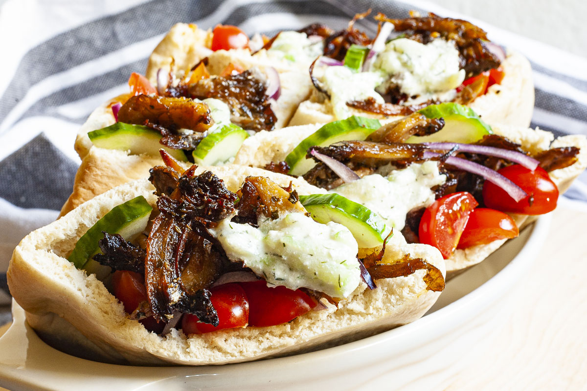 Several pocket on a white serving tray stuffed with crispy brown shredded oyster mushroom, tomato and cucumber slices andwhite-green tzaztziki sauce