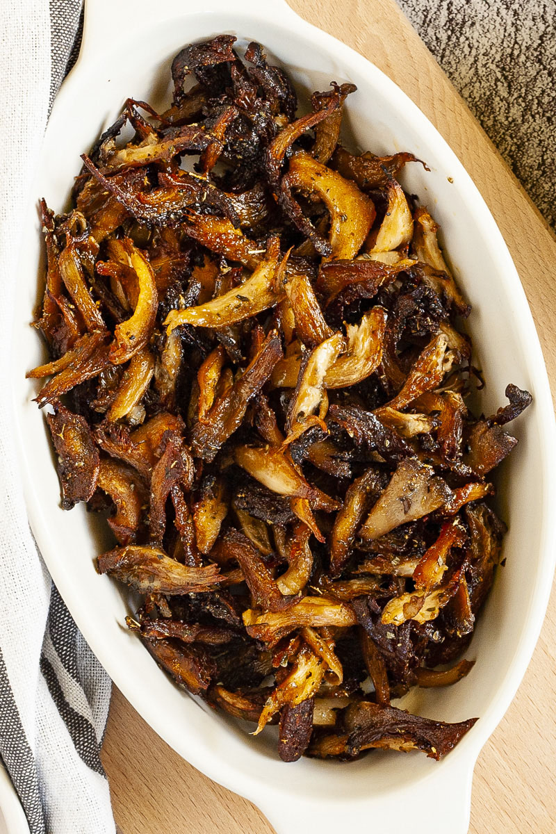 White serving bowl full of dark brown crispy shredded oyster mushrooms