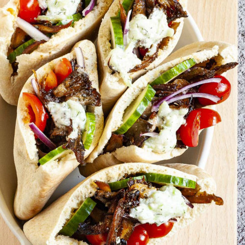 Several pita pocket on a white serving tray stuffed with crispy brown shredded oyster mushroom, tomato and cucumber slices andwhite-green tzaztziki sauce