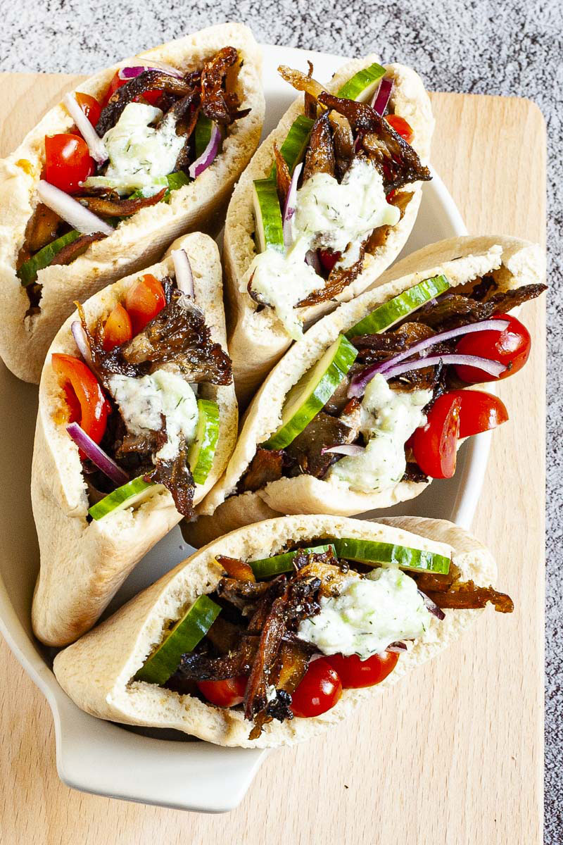 Several pita pocket on a white serving tray stuffed with crispy brown shredded oyster mushroom, tomato and cucumber slices andwhite-green tzaztziki sauce