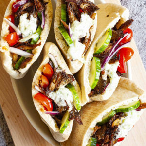 Several pita pocket on a white serving tray stuffed with crispy brown shredded oyster mushroom, tomato and cucumber slices andwhite-green tzaztziki sauce