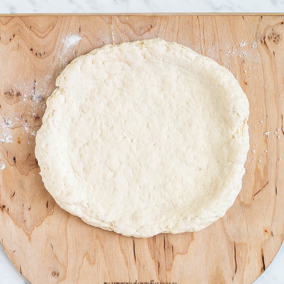 A pizza-shaped dough on a wooden pizza peel.