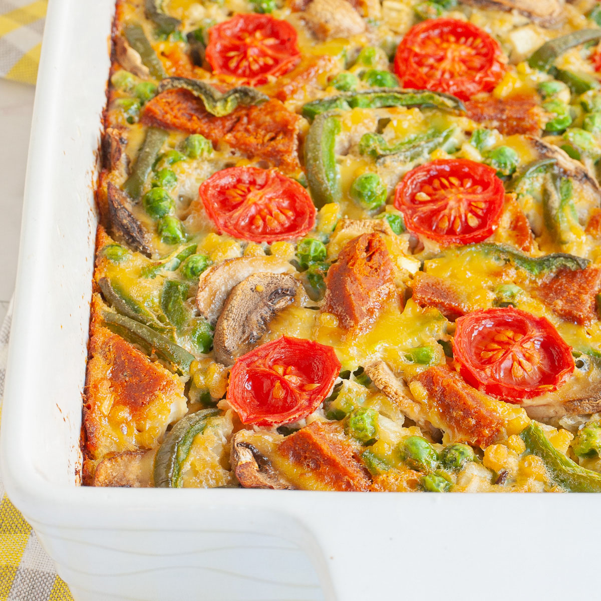 Cherry tomatoes, mushroom slices, bell pepper slices on top of a yellow cake-like dough is in a white casserole dish.