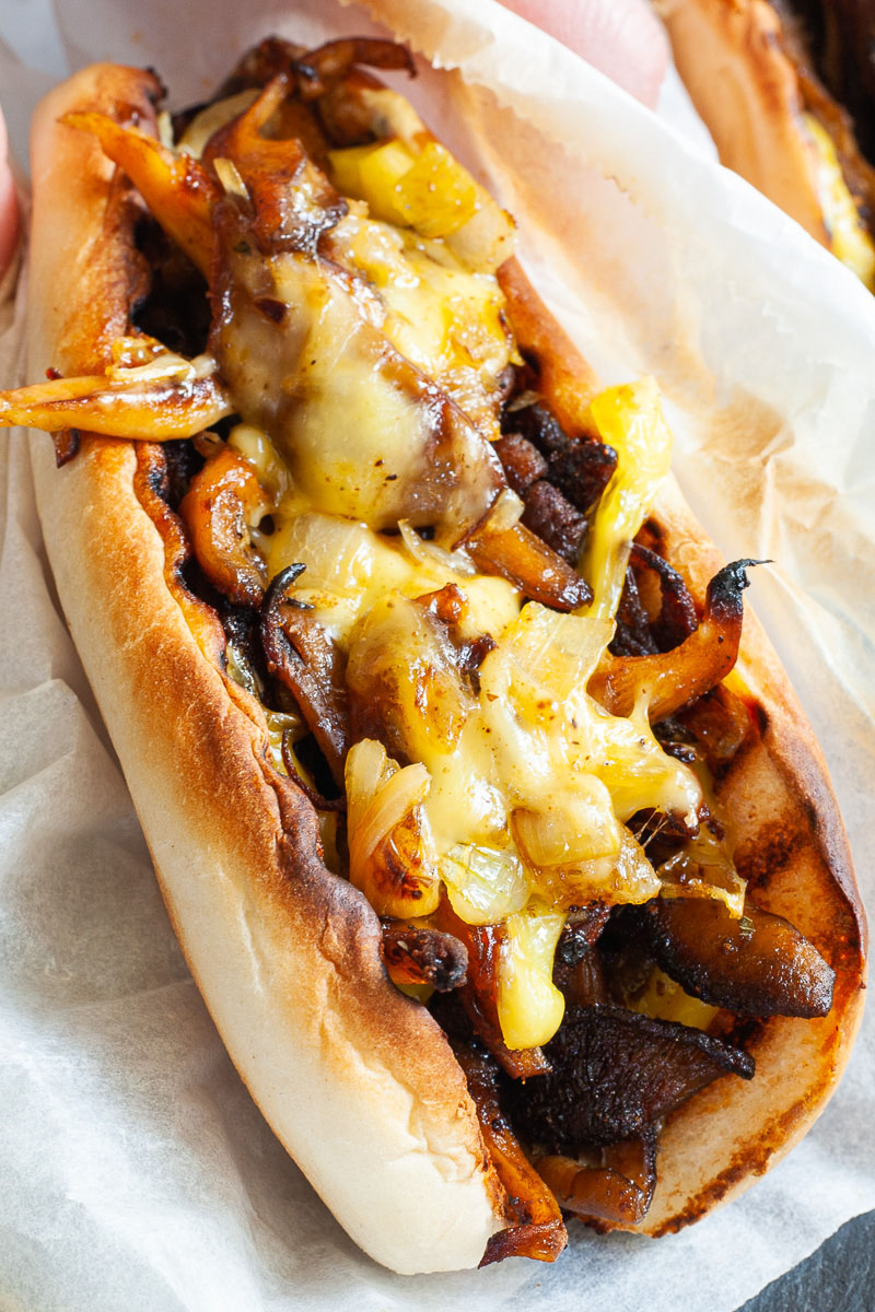 A bread loaf stuffed with brown mushroom shreds and melted cheese wrapped in a white paper.