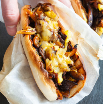 A hand is holding a closed bread loaf stuffed with brown mushroom shreds and melted cheese wrapped in a white paper