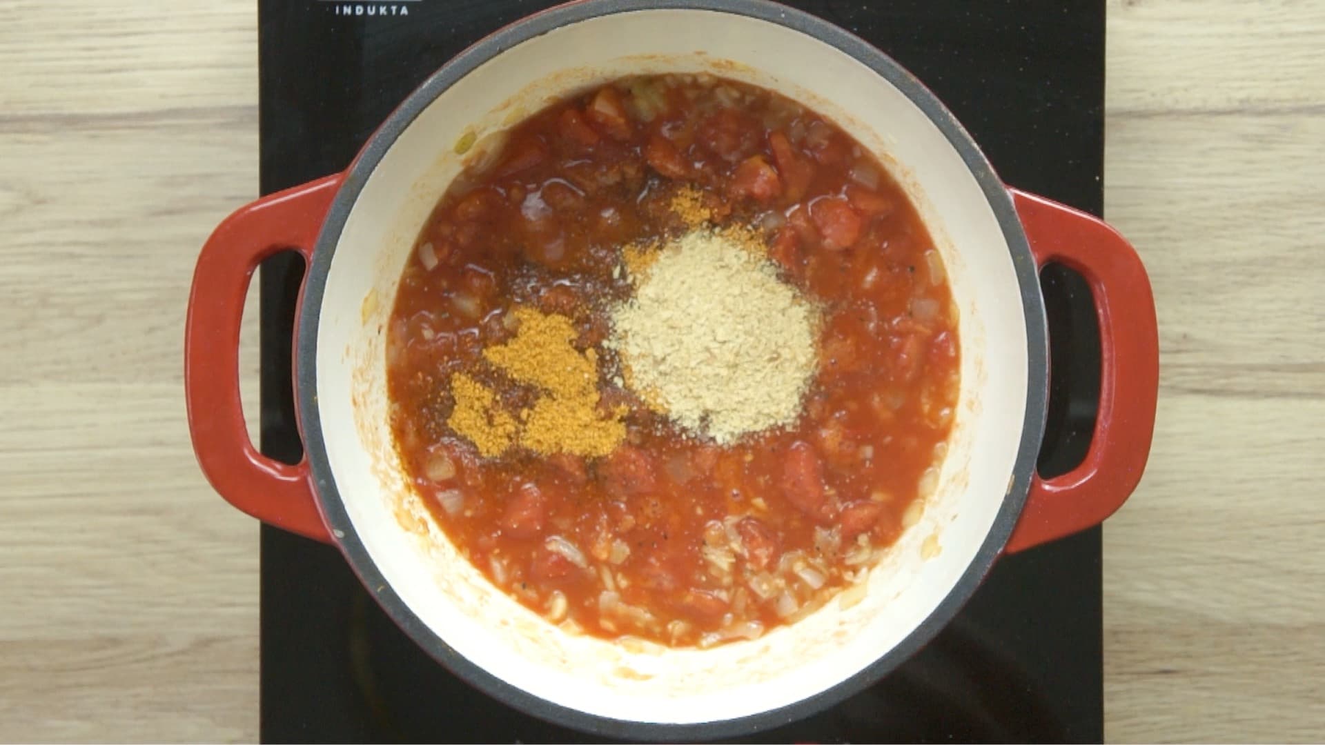 Chopped tomatoes in red sauce, onion and garlic pieces and two heaps of yellow flakes in a red enameled Dutch oven.