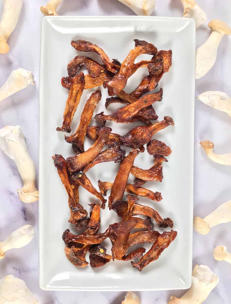 White rectangle plate from above with dark brown crispy mushroom shreds, while the raw mushroom shreds are around the plate in comparison