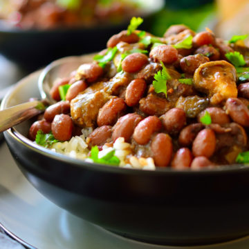 Black bowl with rice topped with beans and mushrooms shreds in a dark brown sauce.