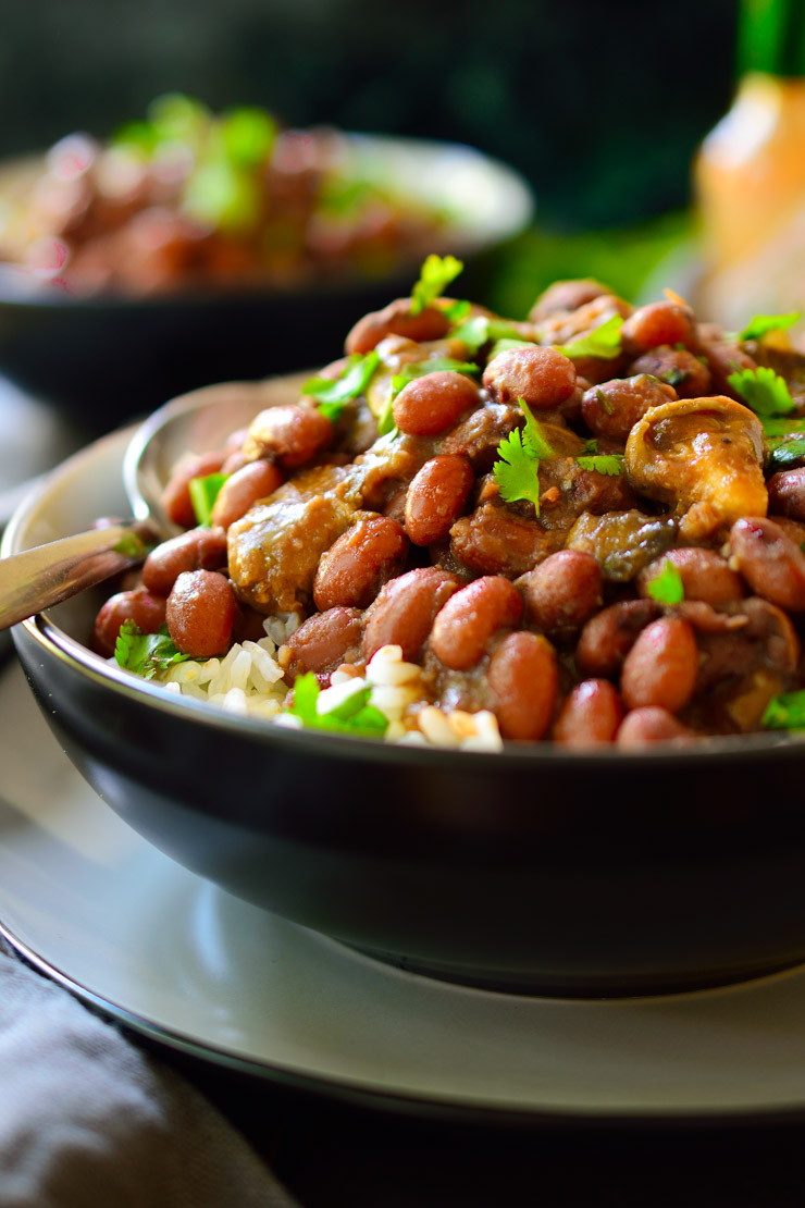 Black bowl with rice topped with beans and mushrooms shreds in a dark brown sauce.