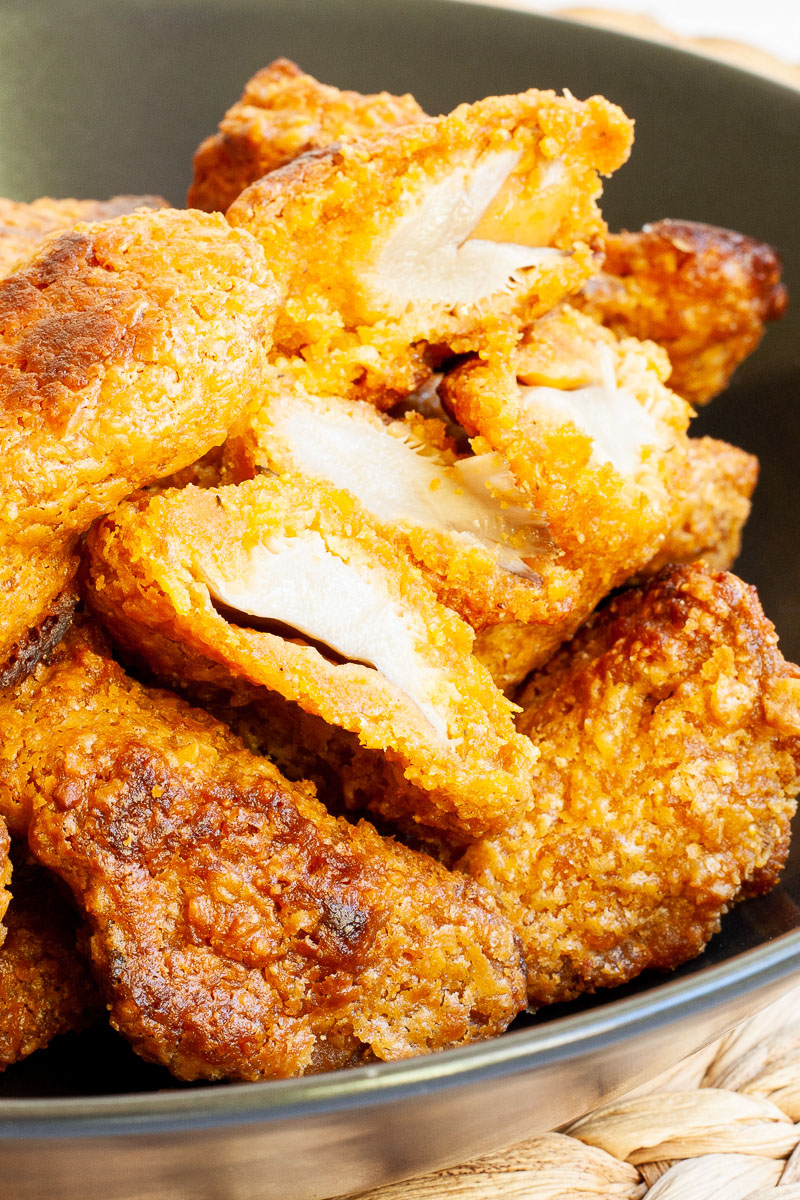 Brown breaded wings in a black bowl. A couple of pieces are cut in half to show a white chicken-like inside.