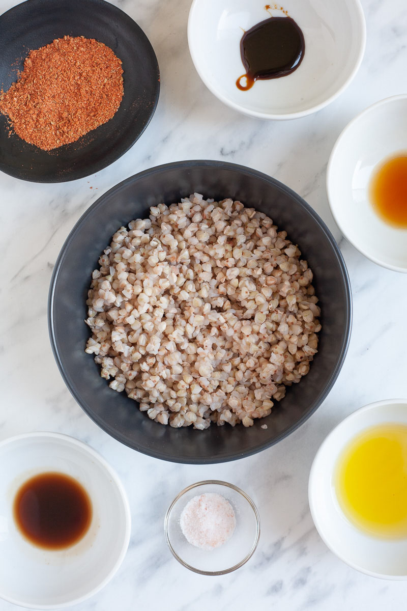 Lots of small bowls with ingredients to make vegan bacon bits like black liquids, red spices, yellow oil and cooked buckwheat seeds