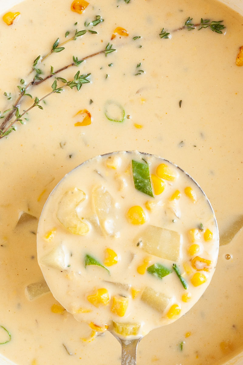 Light yellow soup up very close with a laddle taking a serving. You can see chopped celery, diced potatoes, corn and sliced spring onion