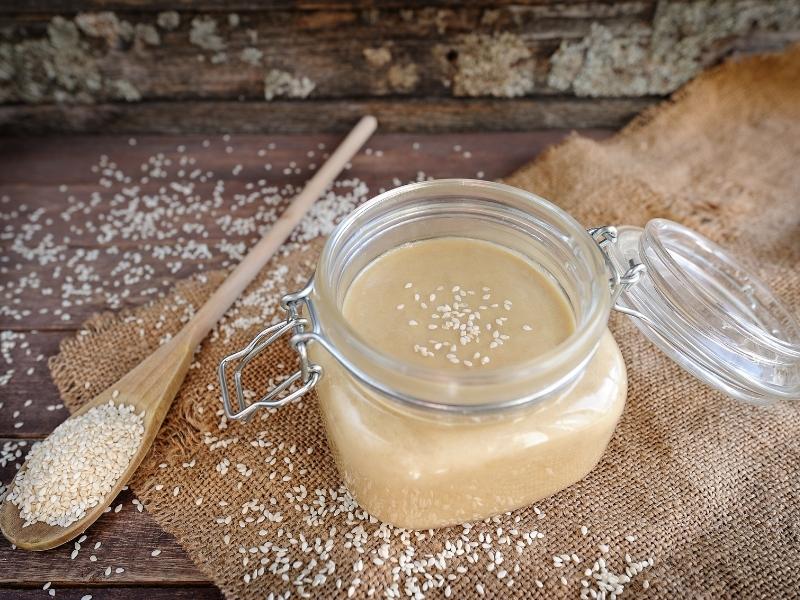 Glass mason jar with light brown paste sprinkled with sesame seeds on a wooden board