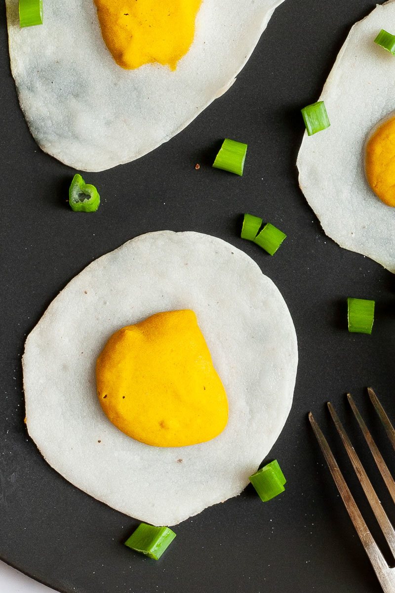 3 fried egg lookalike with white and yolk part on a black plate sprinkled with green spring onion rings.