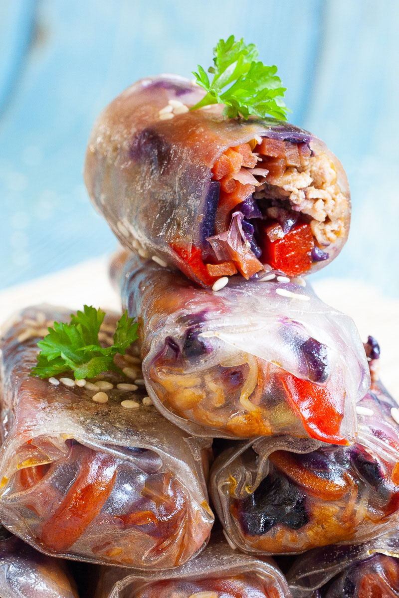 Lots of spring rolls placed on top of each other like a pyramid.The top one is cut in half so you can see inside the purple cabbage bits and some carrot and bell pepper pieces.