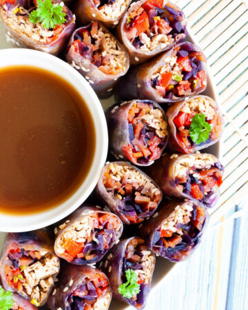 Lots of spring rolls cut in half and arranged in a semi-circular dish facing upwards around a brown dipping sauce.