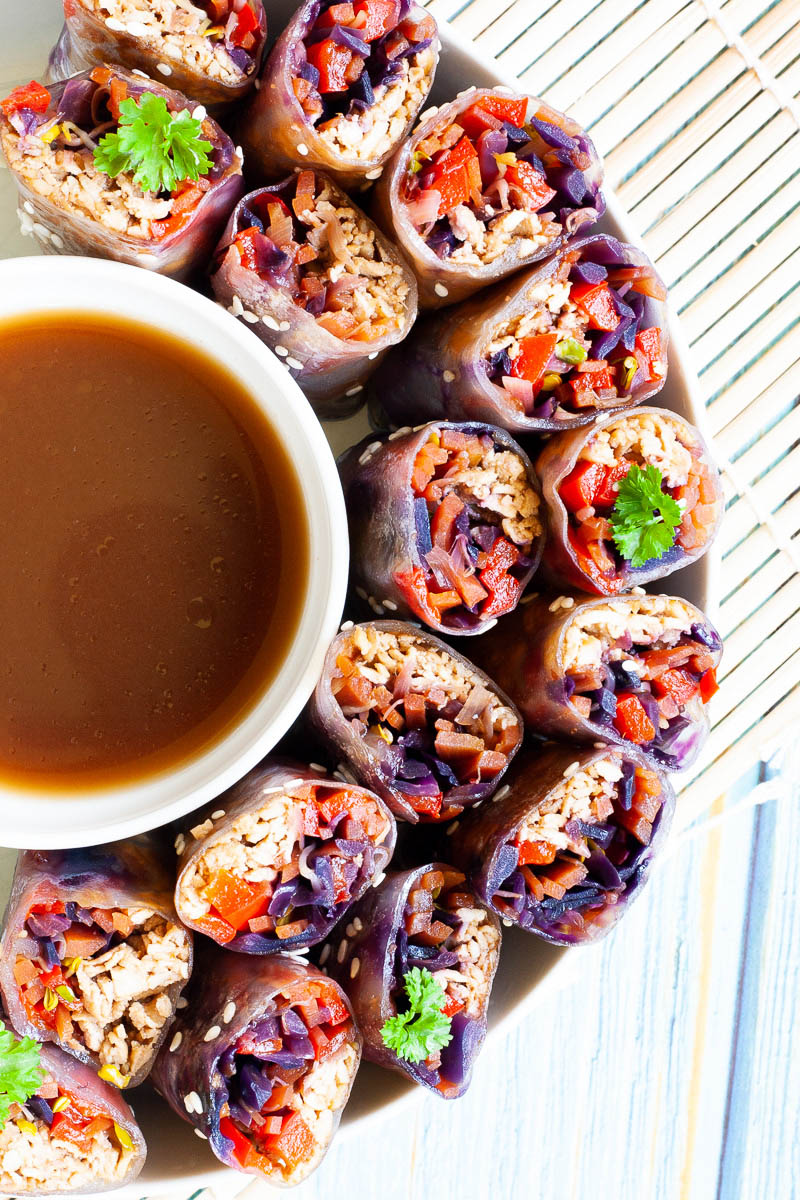 Lots of spring rolls cut in half and arranged in a semi-circular dish facing upwards around a brown dipping sauce.