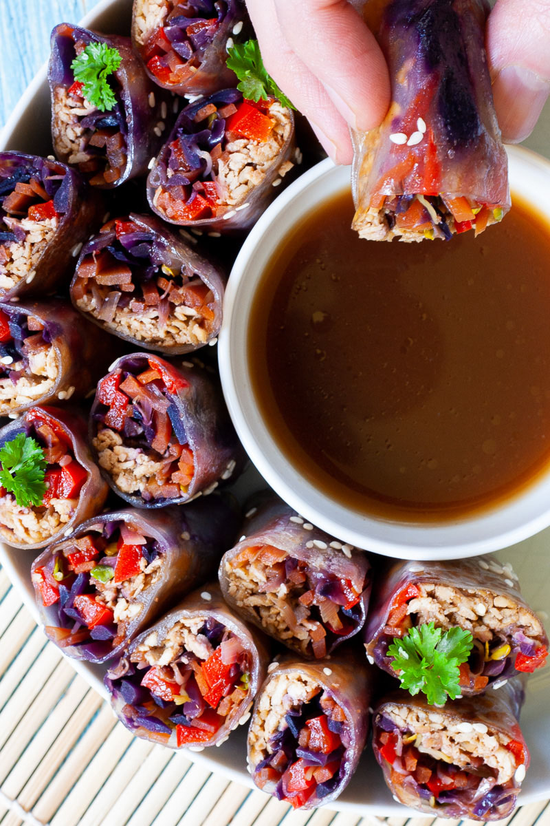 Lots of spring rolls cut in half and arranged in a semi-circular dish facing upwards around a brown dipping sauce. A hand is holding half a spring roll.