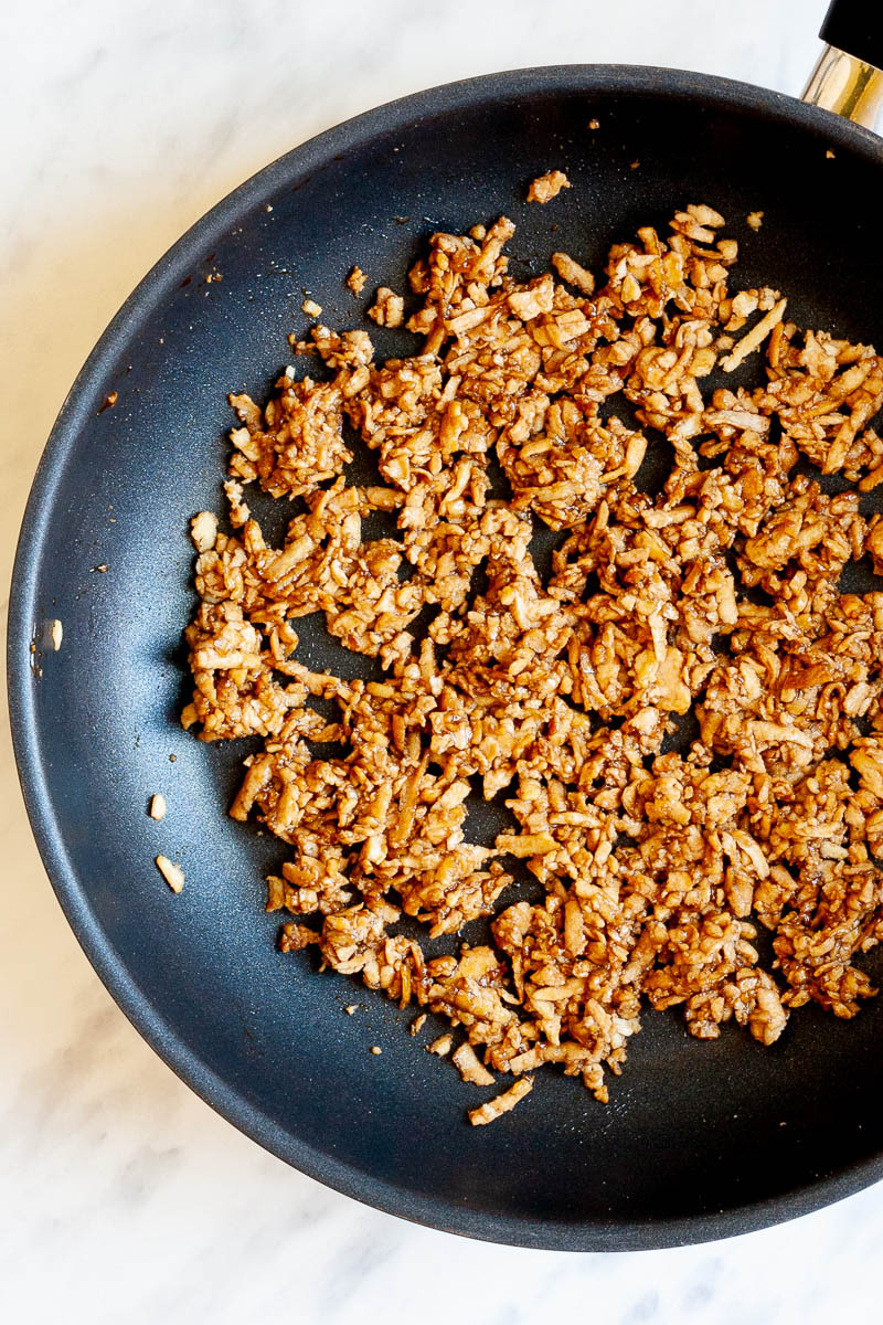 A black frying pan from above with brown shredded tofu.